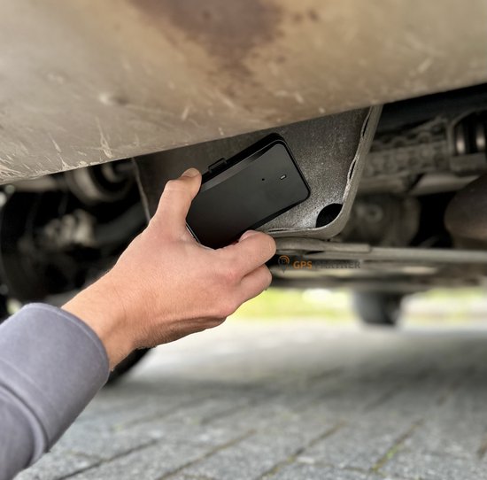 Hand monteert een zwarte Onntrack GPS tracker onder een auto.