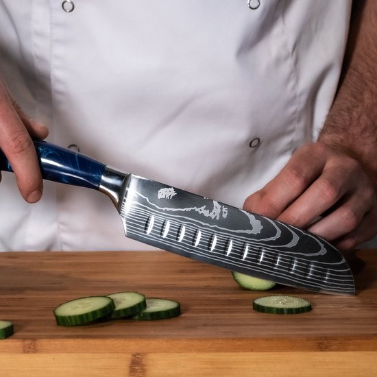 Een chefmes met damascusprint en blauw epoxy handvat snijdt komkommerplakjes op een houten snijplank.