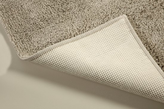 Detail van de antislip onderkant van een beige, pluizige badmat.