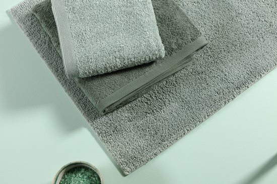 Een stapel zachte, lichtgroene handdoeken en een groene badmat, met een bakje badzout.