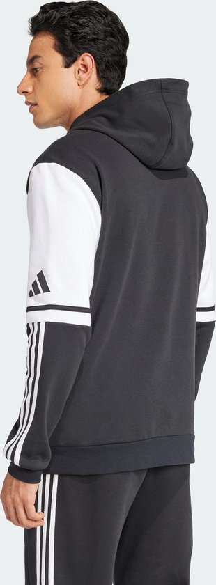 Man met de rug naar ons toe, draagt een donkergrijze capuchontrui met witte mouwen en zwarte Adidas-strepen.