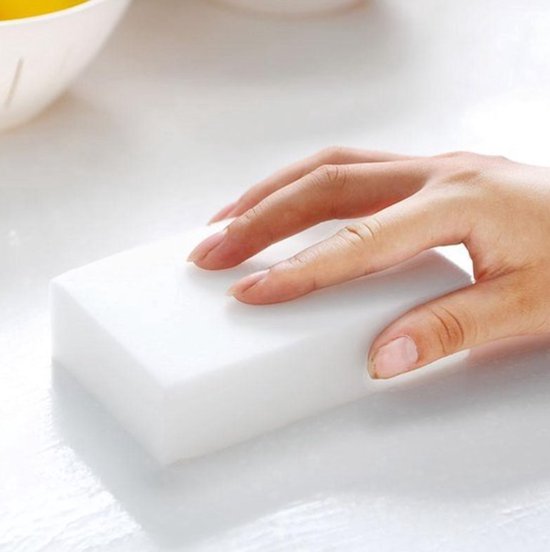 Hand houdt een witte melamine spons vast op een wit oppervlak.