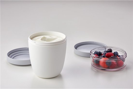 Witte lunchpot met yoghurt en een apart compartiment met bessen.