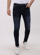 Man in donkerblauwe slim fit jeans met distressed effect en scheuren, gedragen met witte sneakers.