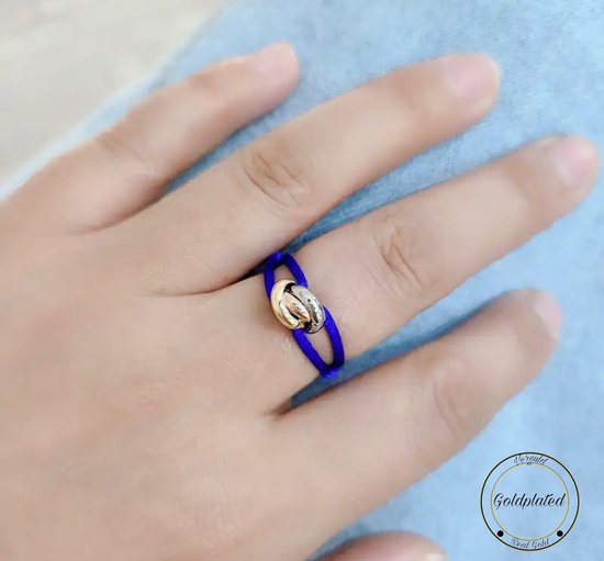 Gouden knoopdetail op een kobaltblauwe band, gedragen op een vinger.
