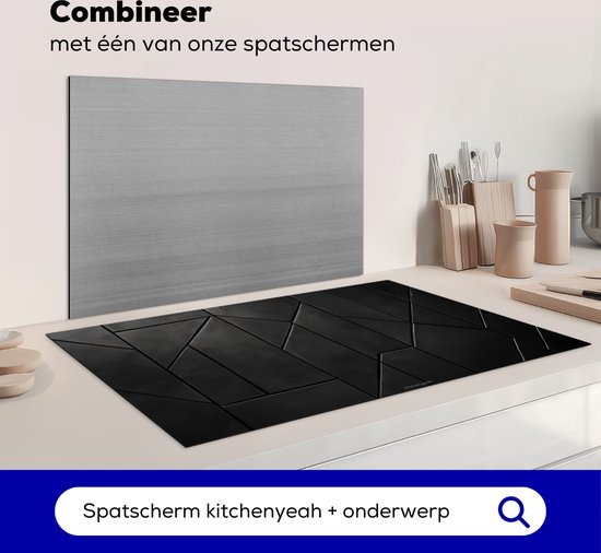 Zwarte inductiebeschermer met geometrisch patroon naast een grijze spatwand op een aanrecht met een inductiekookplaat.