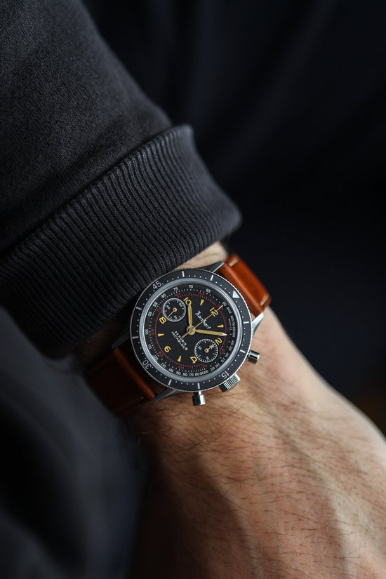 Hanhart horloge met bruine band gedragen om een pols, zwarte wijzerplaat met rode accenten.