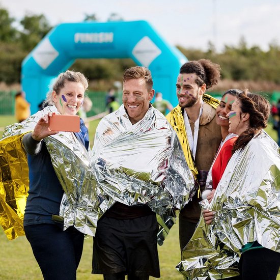 Vrolijke groep van vijf personen met gezichtsverf, die selfies maken na een race, omwikkeld met gouden en zilveren nooddekens.