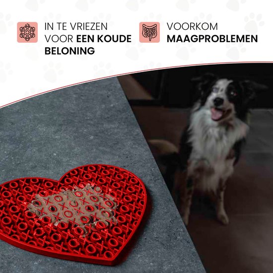 Rode hartvormige likmat met voedsel op een grijze tafel, met een border collie op de achtergrond.