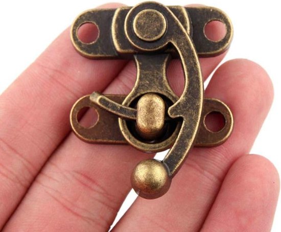 Bronzen antieke kistsluiting met gebogen haakje en knopje, vastgehouden in een hand.