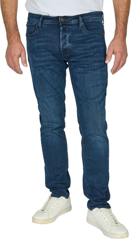 Man van voren, gekleed in een donkerblauwe slim fit spijkerbroek en witte sneakers.