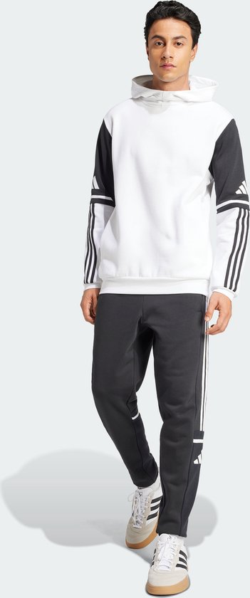 Man met een wit sweatshirt met donkergrijze mouwen en Adidas-strepen op de mouwen, staand.
