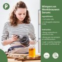 Vrouw met krullend bruin haar maakt wimpers en wenkbrauwen serum met mortier en stamper.