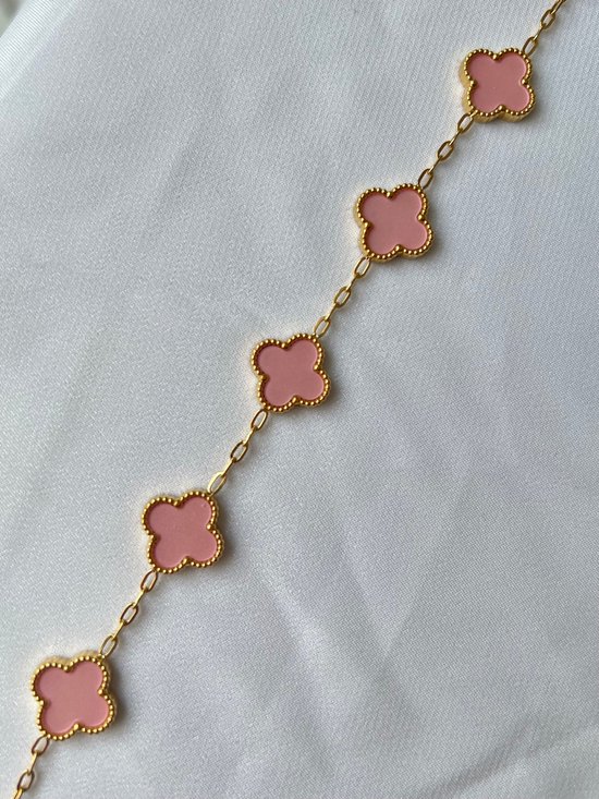 Gouden armband met roze klaverbedels op een witte, geplooide stof.