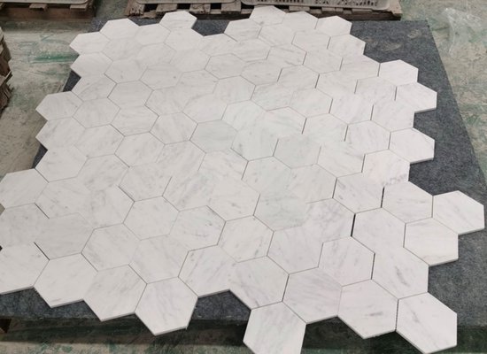 Een vel met witte marmeren hexagon mozaïektegels, geplaatst op een donkergrijze ondergrond.