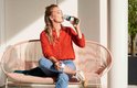 Vrouw in oranje blouse drinkt uit een Mepal waterfles met groene band.