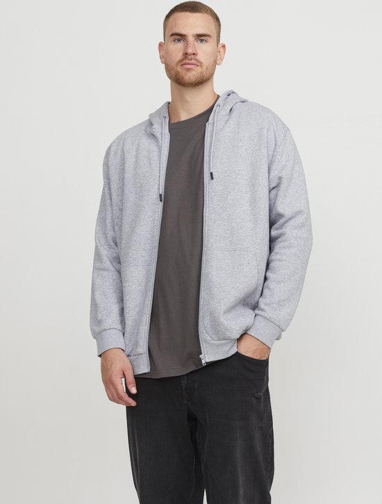 Man draagt een lichtgrijs vest met rits en capuchon over een donkergrijs T-shirt en een zwarte jeans.