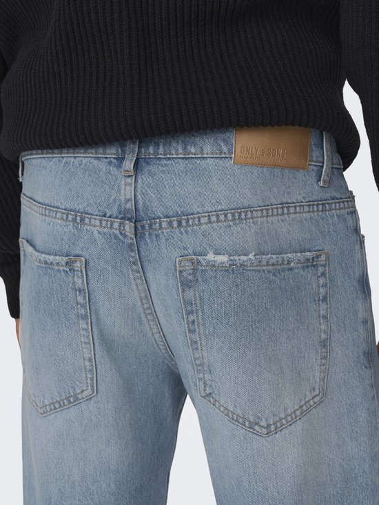 Close-up van de achterkant van een lichtblauwe jeans met distressed details en een bruin merklabel.