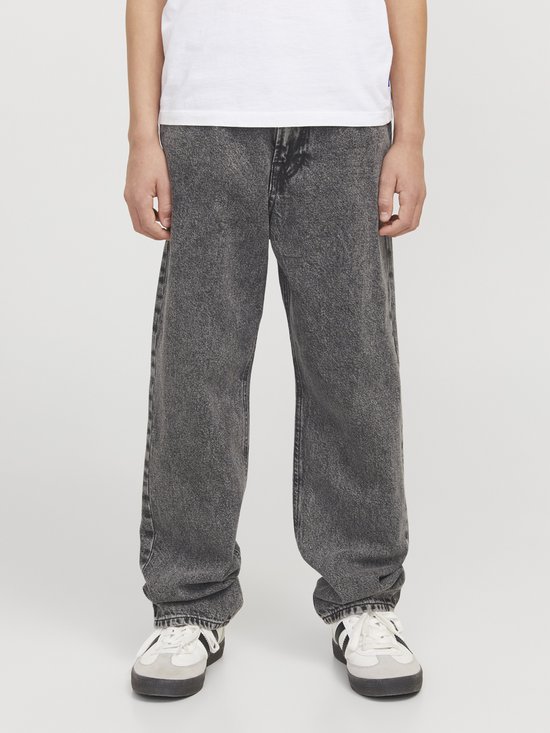 Jongen in grijze wijde jeans met stonewashed wassing en witte sneakers.