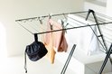 Zwart wasknijpertasje hangend aan een zwart Brabantia HangOn droogrek, naast een beige top en witte handdoek.