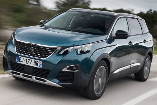 Een tealgroene Peugeot 5008 rijdt over een weg, gezien vanaf de voorkant rechts. De auto heeft getinte ramen en zilverkleurige accenten.