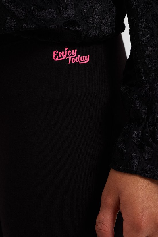 Close-up van een zwarte legging met roze tekst "Enjoy Today".
