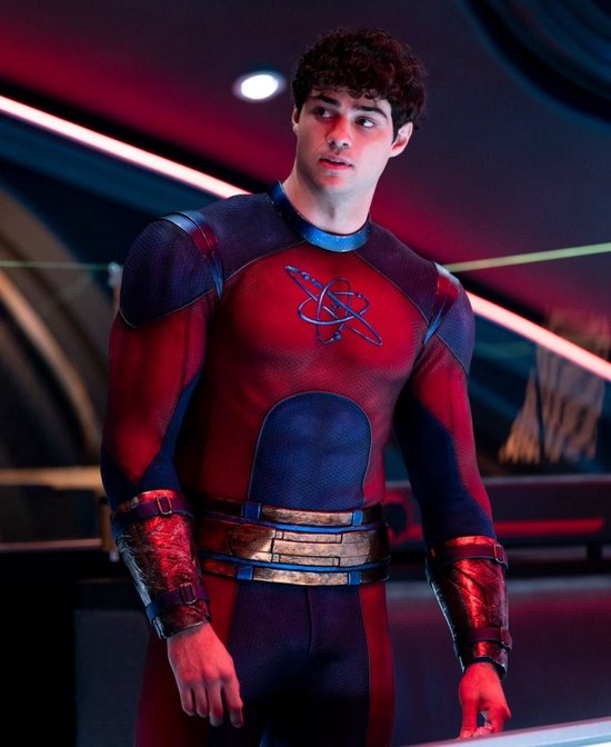 Noah Centineo als Atom Smasher, in een rood en blauw superheldenpak met een atoom symbool op de borst.