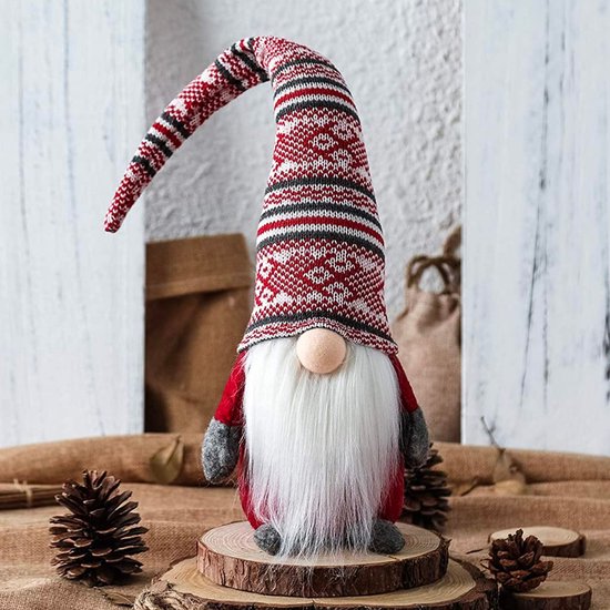 Nain de Noël avec un long bonnet pointu en tricot rouge, blanc et gris à motifs et une barbe blanche, debout sur une tranche de bois.