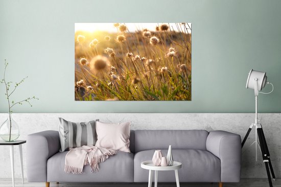 Une peinture de fleurs séchées sous la lumière dorée du soleil, suspendue au-dessus d'un canapé gris.