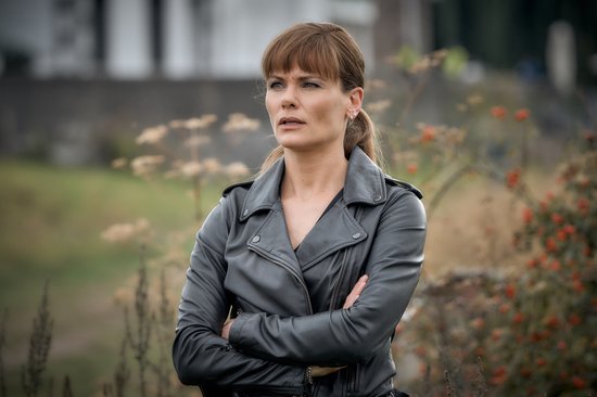 Een vrouw met een leren jas staat met gekruiste armen in de buitenlucht.