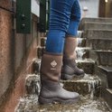 Persoon in blauwe jeans, staand op natte stenen trap, draagt bruine Muck Boot Derwent II laarzen.