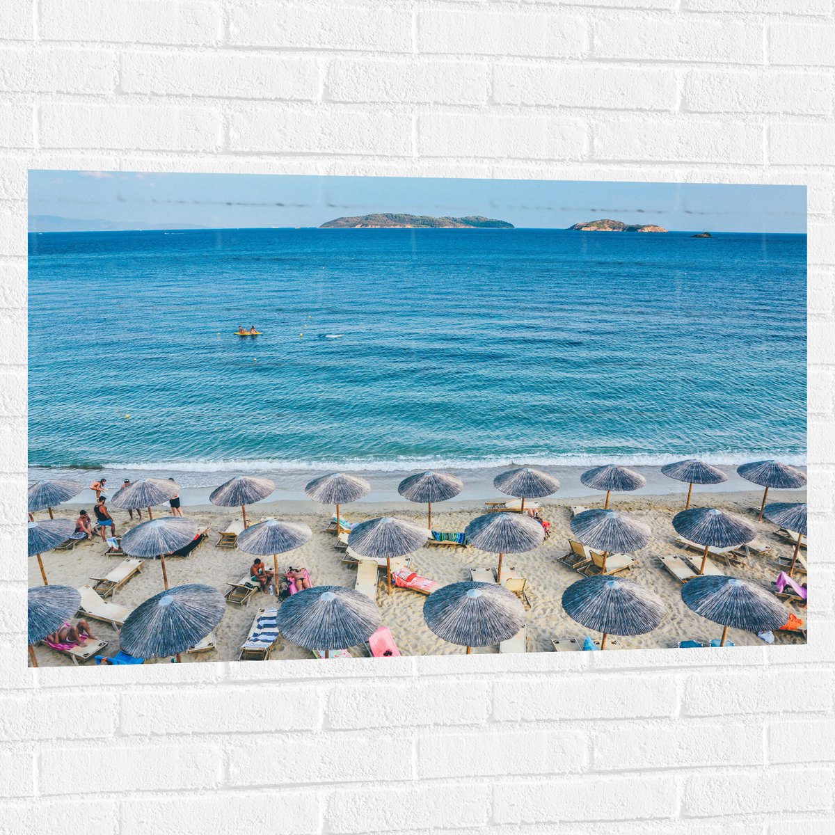 Muursticker - Rieten Parasols met Ligbedjes op het Strand - 105x70 cm Foto op Muursticker