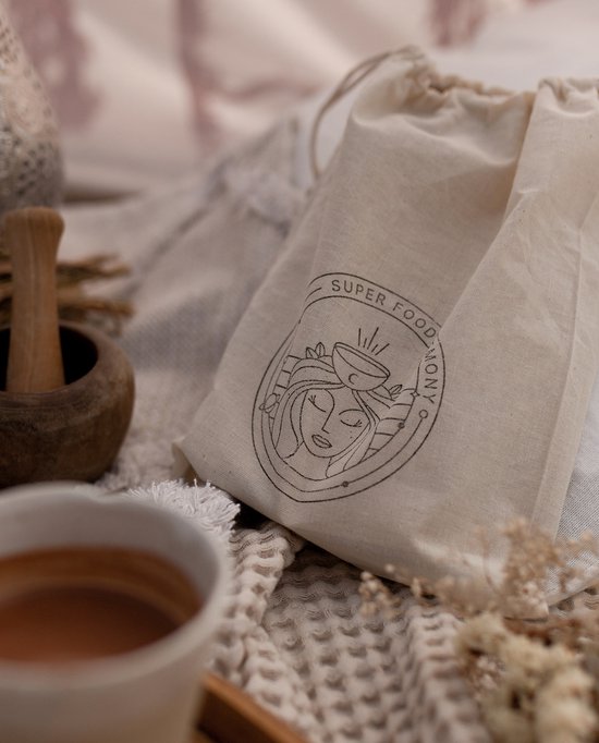 Een gebreide deken met daarop een beige canvas tas met een cirkelvormig logo van een gezicht, omlijst door tekst.