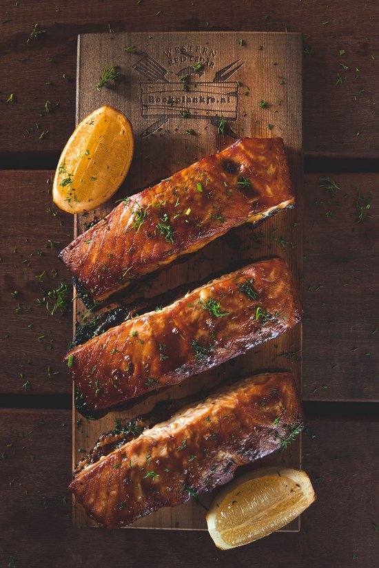Drie stukken gegrilde zalm op een cederhouten plank, gegarneerd met dille en citroen.