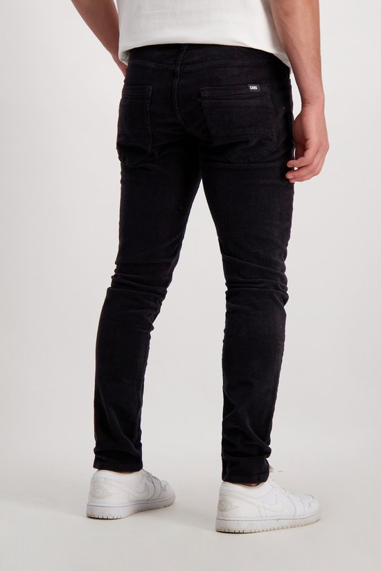 Man met zwarte corduroy broek, zichtbaar van achteren, met witte sneakers.