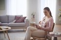Vrouw zit op stoel met Philips Avent borstkolf en telefoon.