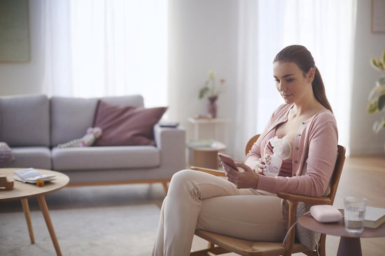 Vrouw zit op stoel met Philips Avent borstkolf en telefoon.