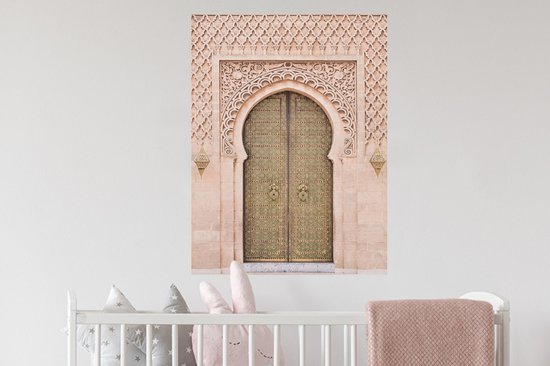 Une porte marocaine couleur sable avec des détails dorés et une sculpture sur pierre complexe, accrochée au-dessus d'un lit de bébé.