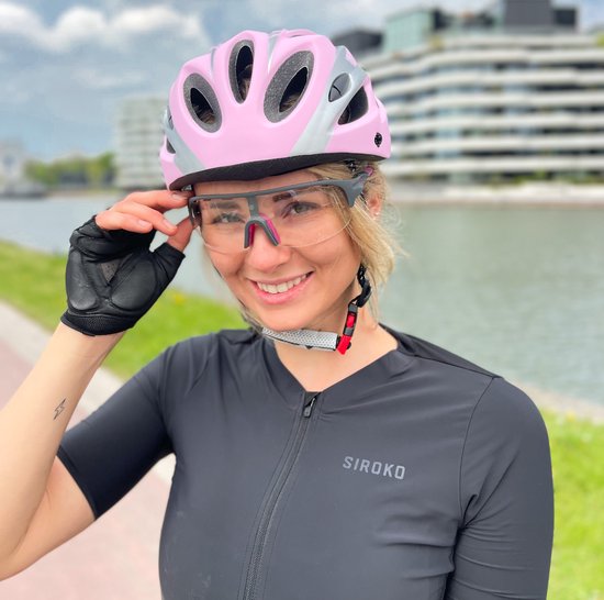 Vrouw met blonde paardenstaart draagt een roze en zilveren fietshelm, een zwarte sportshirt en een transparante bril.