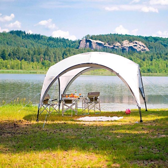 Een witte Coleman partytent bij een meer, met een tafel en stoelen erin.
