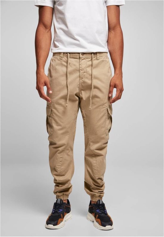 Man in beige cargo broek met trekkoord, voorkant zichtbaar, met zakken en elastische enkelbanden.