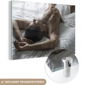 MuchoWow® Glasschilderij 60x40 cm - Schilderij acrylglas - Getinte man bedekt zich met een deken - Foto op glas - Schilderijen