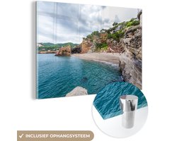 MuchoWow® Glasschilderij 90x60 cm - Schilderij acrylglas - Strand met rotsen bij Costa Brava - Foto op glas - Schilderijen