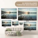 Différentes tailles d'une peinture d'un lever de soleil sur un lac brumeux, placées au-dessus d'un canapé et d'un bureau.