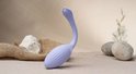Vibrateur côtelé lilas clair en forme de cygne, sur fond sableux avec des pierres