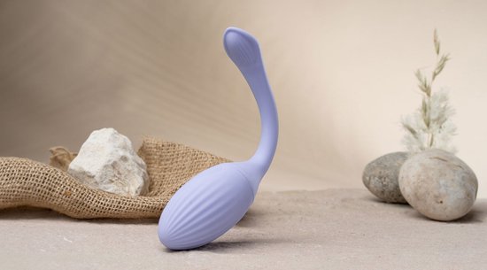 Vibrateur côtelé lilas clair en forme de cygne, sur fond sableux avec des pierres
