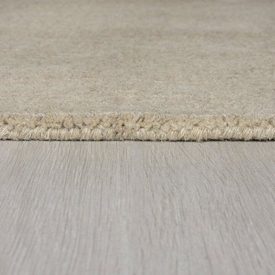 Close-up van de rand van een lichtbeige vloerkleed met een grovere textuur langs de rand.
