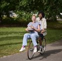 Een man en vrouw rijden op een fiets in een park, de vrouw draagt een stapel gekleurde mokken.