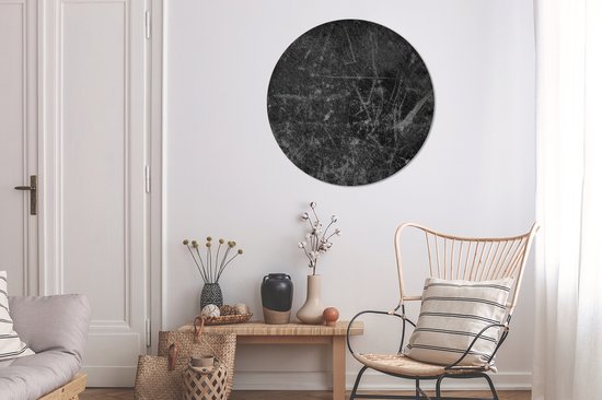 Décoration murale ronde noire aspect cuir et griffes, au-dessus d'une table d'appoint en bois avec vases et fauteuil en rotin.