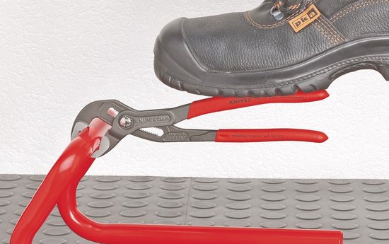 Een voet drukt op een Knipex Cobra waterpomptang die een rode buis vasthoudt.